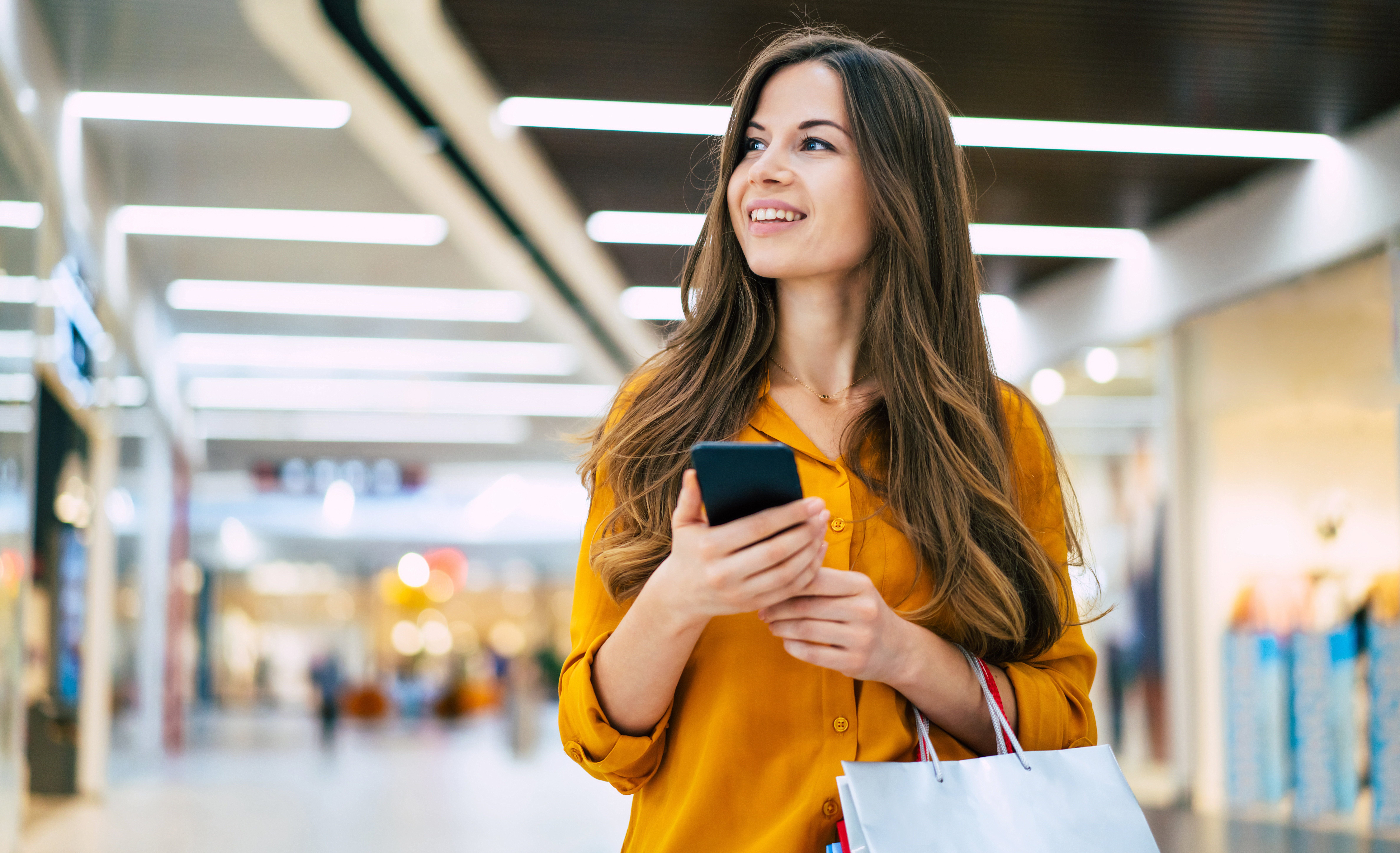 Femme en chemise jeune dans un centre commercial avec un téléphone et un sac à la main