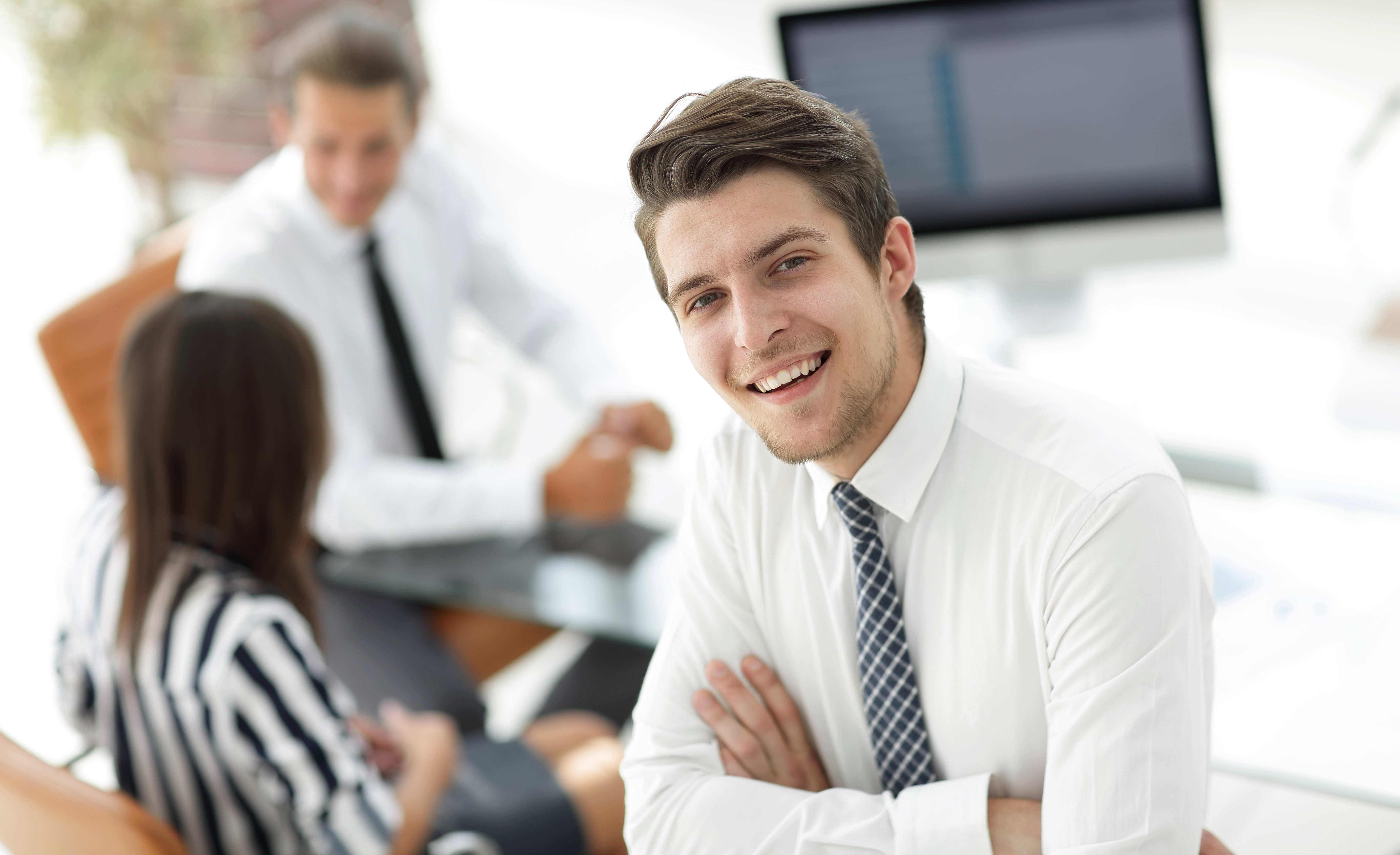 Homme souriant devant une table avec une femme et un homme assis à un bureau